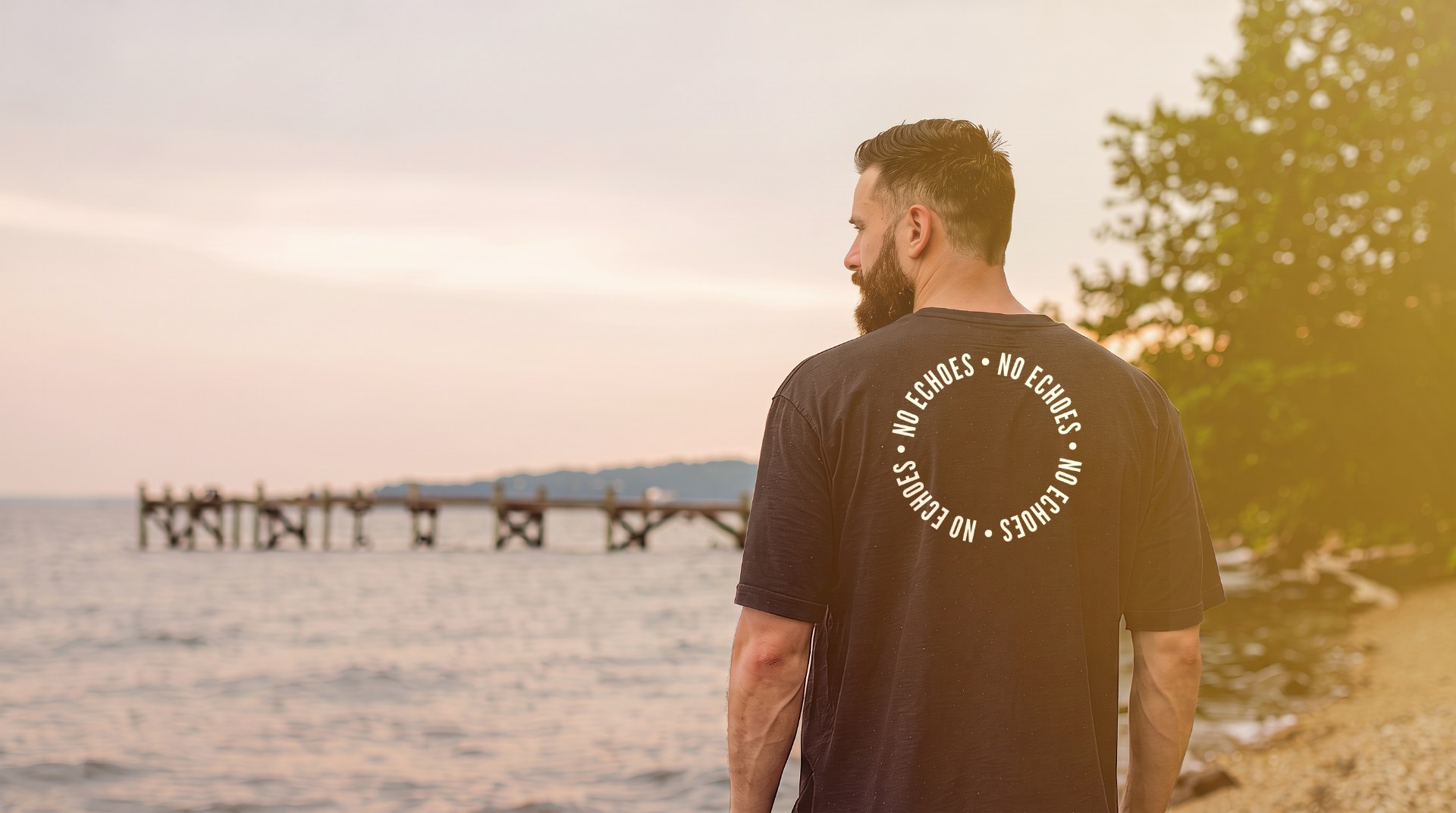 Back view of a person wearing a black shirt with the circular NO ECHOES mark beside the water.